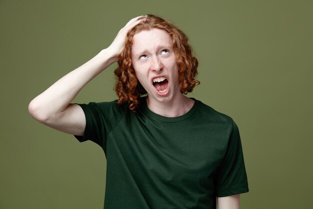 Ontevreden kijken naar het opsteken van de hand op het hoofd jonge knappe kerel met een groen t-shirt geïsoleerd op een groene achtergrond