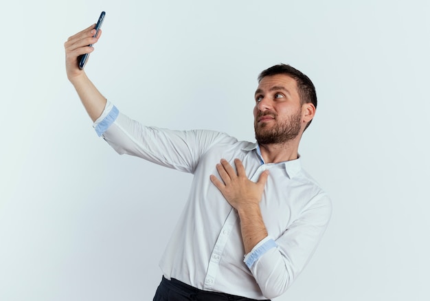 Ontevreden knappe man legt hand op de borst kijken naar telefoon geïsoleerd op een witte muur