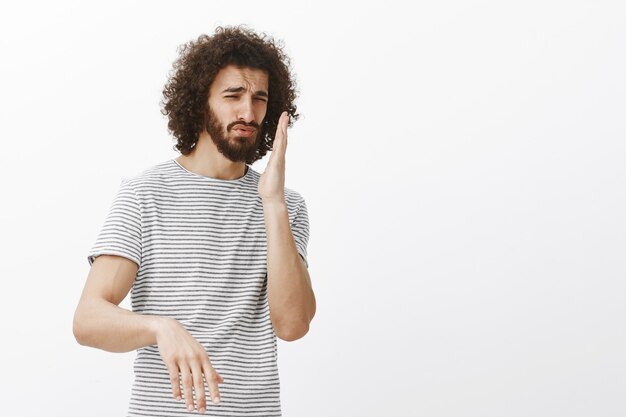 Ontevreden knappe Spaanse man in gestreept t-shirt, zwaaiende handpalm dichtbij neus en fronsend, vreselijke geur ruikend