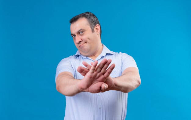 Ontevreden man van middelbare leeftijd in blauw verticaal gestreept overhemd dient afwijzing op een blauwe ruimte in