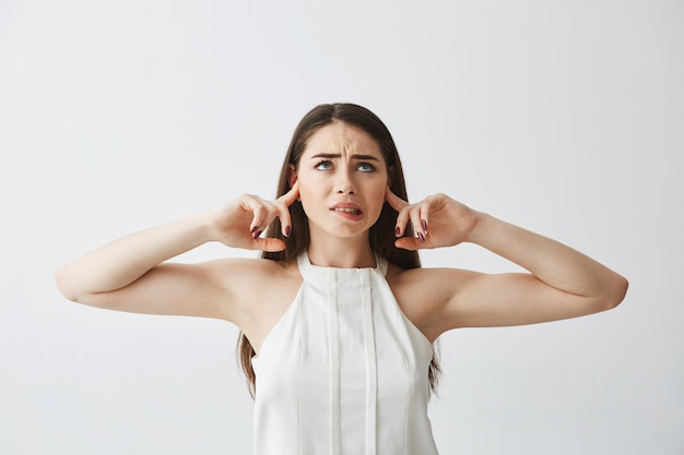 Ontevreden mooie brunette meisje sluitende oren met vingers van lawaai bijten lip.