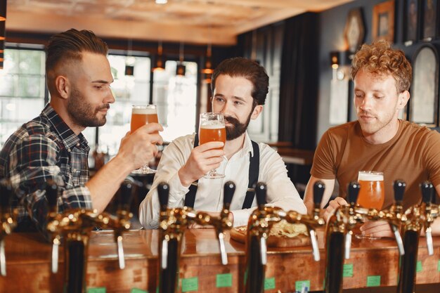 Ontmoeting met de beste vrienden. Drie gelukkige jonge mannen in vrijetijdskleding praten en bier drinken zittend in de bar samen.