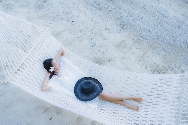 Ontspan de portret mooie jonge aziatische vrouwenzitting op hangmat rond overzeese strandoceaan voor