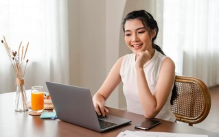 Ontspan jonge aziatische zakenvrouw die uit het raam kijkt en aan laptopcomputer werkt