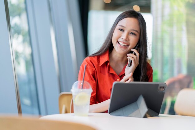 Ontspan vrije tijd aantrekkelijke slimme aziatische vrouwelijke freelance ondernemer glimlach en geniet van het werken met smartphone en laptop in café met vervagen stad zakelijke digitale nomade casual ideeën concept