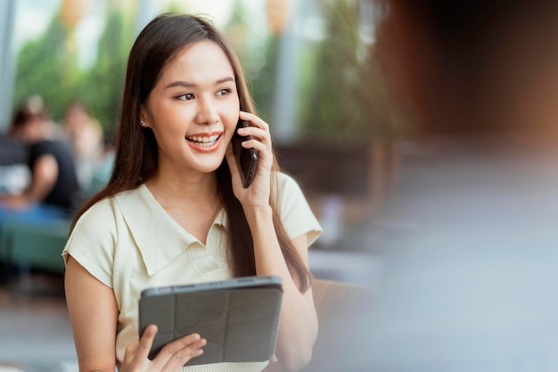 Ontspan vrije tijd aantrekkelijke slimme aziatische vrouwelijke freelance ondernemer glimlach en geniet van het werken met smartphone en laptop in café met vervagen stad zakelijke digitale nomade op afstand werken casual ideeën concept