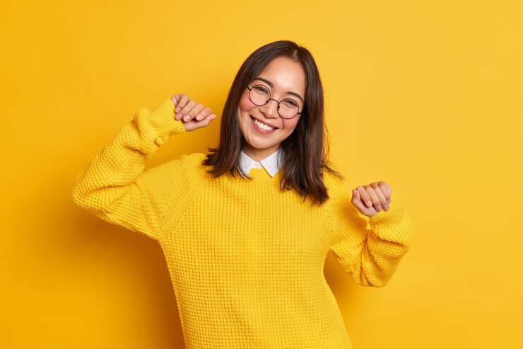 Gratis Foto ontspannen brunette mooie vrouw met oosterse uitstraling heft armen en glimlach aangenaam kantelt hoofd heeft positieve gezichtsuitdrukking draagt warme trui.