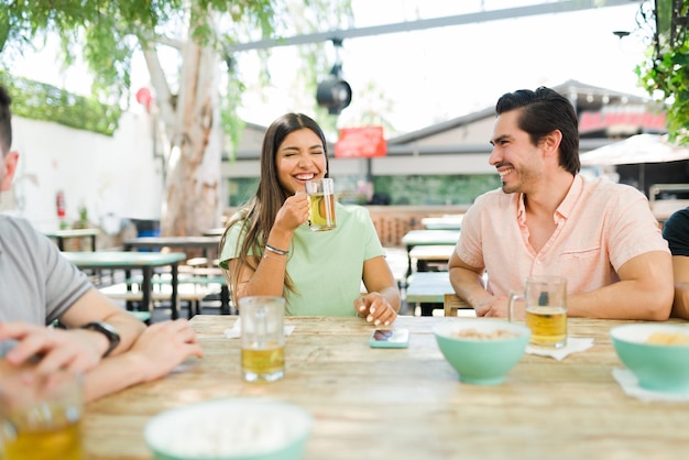 Ontspannen jonge vrouw die lacht om een grappig verhaal van haar vriend. Goede vrienden maken grapjes terwijl ze genieten van koud bier en drankjes aan de bar