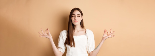 Gratis foto ontspannen jonge vrouw mediterend hand in hand in yoga zen pose en gesloten ogen voelen vrede en glimlachen