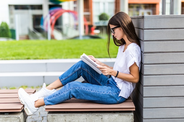 Ontspannen vrouw die een hardcoverboek leest bij zonsondergangzitting op een bank