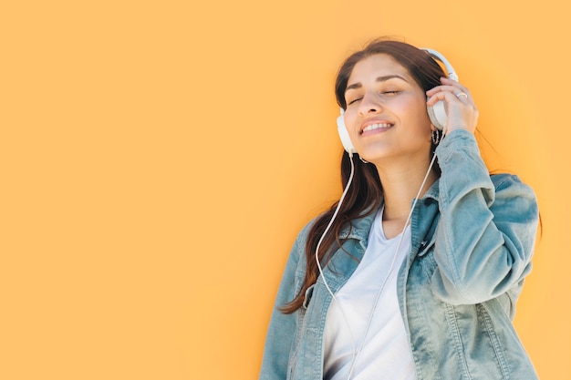 Gratis foto ontspannen vrouw het luisteren muziek tegen gele achtergrond