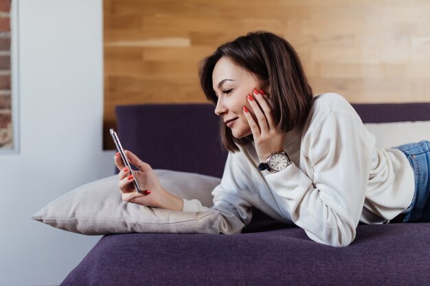 Ontspannen vrouw met behulp van een slimme telefoon liggend op een bed thuis