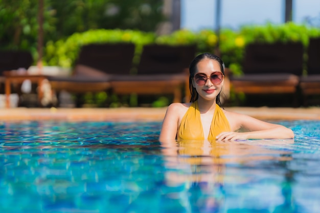 Ontspant de mooie jonge Aziatische vrouwen van het portret glimlach en gelukkig rond zwembad in hoteltoevlucht