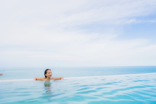 Ontspant de portret jonge Aziatische vrouw glimlach gelukkig rond openluchtzwembad in hoteltoevlucht met overzeese oceaanmening