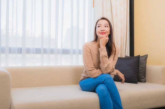Ontspant de portret mooie jonge aziatische vrouw glimlach gelukkig op het binnenland van de bankdecoratie van slaapkamer