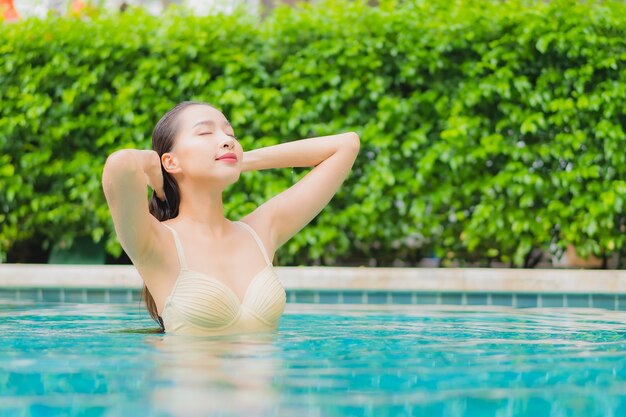 Ontspant de portret mooie jonge aziatische vrouw glimlach rond openluchtzwembad in hoteltoevlucht