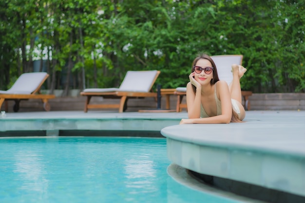 Ontspant de portret mooie jonge aziatische vrouw glimlach rond openluchtzwembad