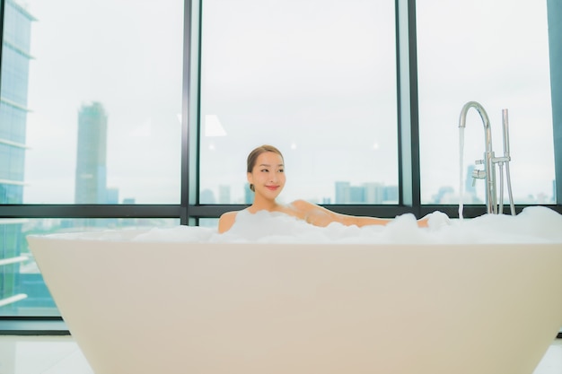 Ontspant de portret mooie jonge aziatische vrouw glimlachvrije tijd in badkuip in badkamersbinnenland