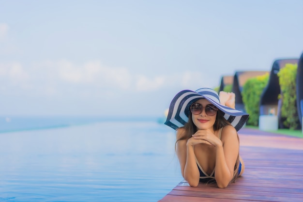 Gratis foto ontspant de portret mooie jonge aziatische vrouw rond zwembad in hoteltoevlucht