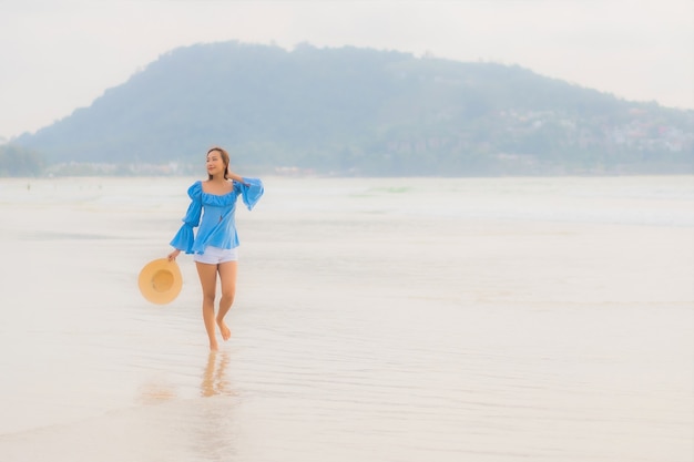 Ontspant de portret mooie jonge Aziatische vrouw vrijetijdsglimlach rond strand overzeese oceaan in zonsondergangtijd