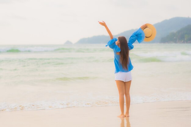 Ontspant de portret mooie jonge Aziatische vrouw vrijetijdsglimlach rond strand overzeese oceaan in zonsondergangtijd