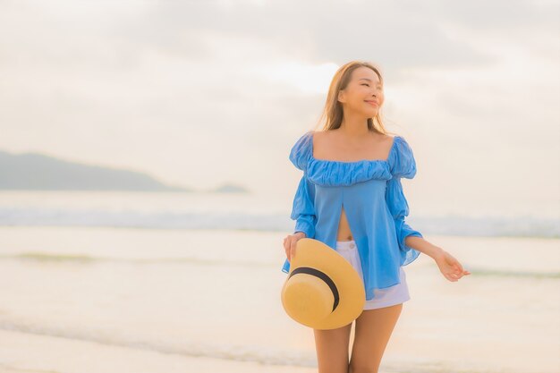 Ontspant de portret mooie jonge Aziatische vrouw vrijetijdsglimlach rond strand overzeese oceaan in zonsondergangtijd