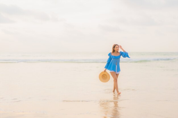 Ontspant de portret mooie jonge Aziatische vrouw vrijetijdsglimlach rond strand overzeese oceaan in zonsondergangtijd