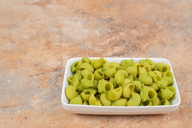 Onvoorbereide groene macaroni in witte plaat op marmeren achtergrond. hoge kwaliteit foto