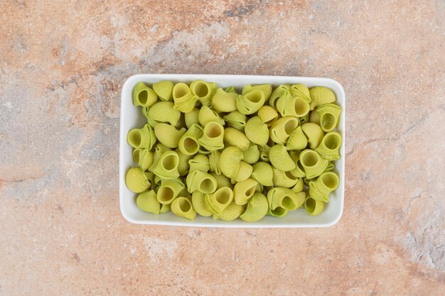 Onvoorbereide groene macaroni in witte plaat op marmeren ruimte.