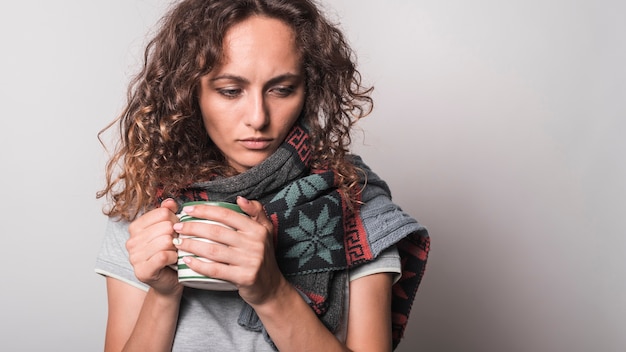 Onwel jonge vrouw met sjaal rond haar hals die koffiemok houdt