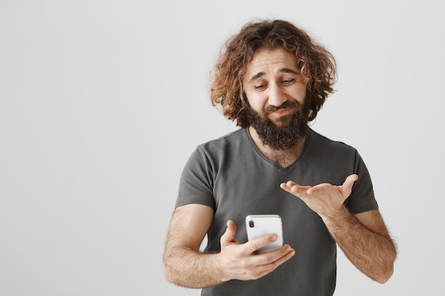 Onzekere man uit het Midden-Oosten die besluiteloos naar mobiele telefoon kijkt, aarzelend