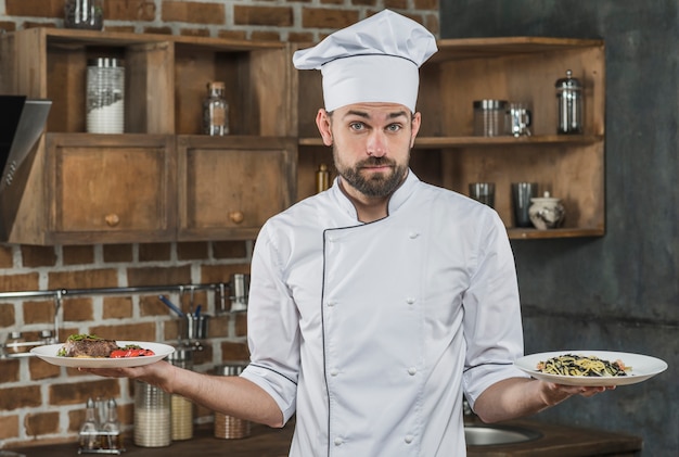 Onzekere mannelijke chef-kok die twee verschillende schotel op zijn hand houdt