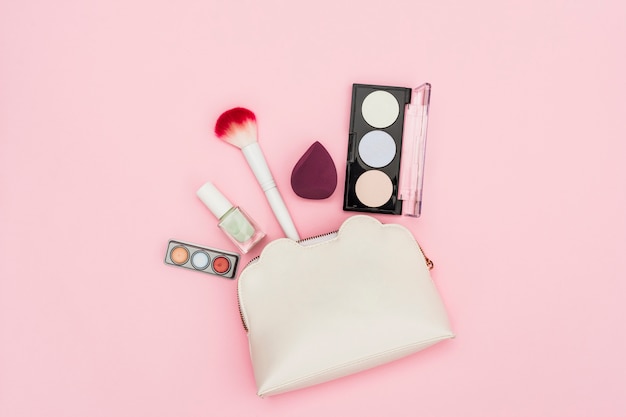 Oogschaduw palet; nagellakfles; blender; make-up borstel en make-up tas op roze achtergrond