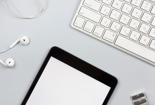 oortelefoon; lege digitale tablet; puntenslijper en wit toetsenbord op grijze achtergrond