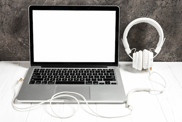 Open laptop met witte hoofdtelefoon op bureau tegen concrete muur