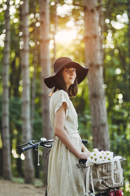 Openluchtportret van aantrekkelijk jong brunette in een hoed op een fiets.