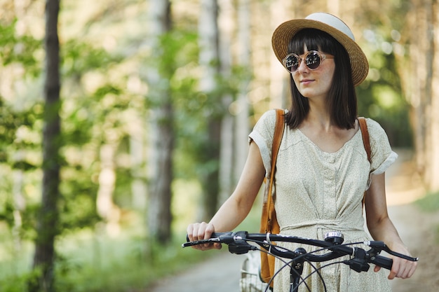Openluchtportret van aantrekkelijk jong brunette in een hoed op een fiets.