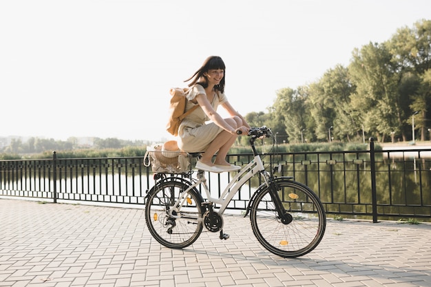 Openluchtportret van aantrekkelijk jong brunette in een hoed op een fiets.