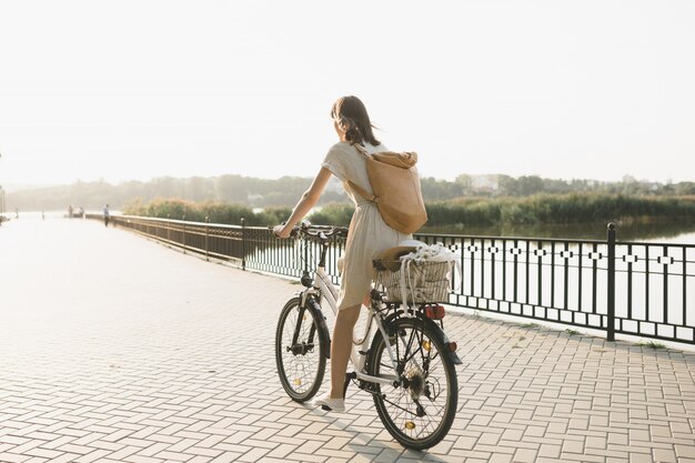 Openluchtportret van aantrekkelijk jong brunette in een hoed op een fiets.