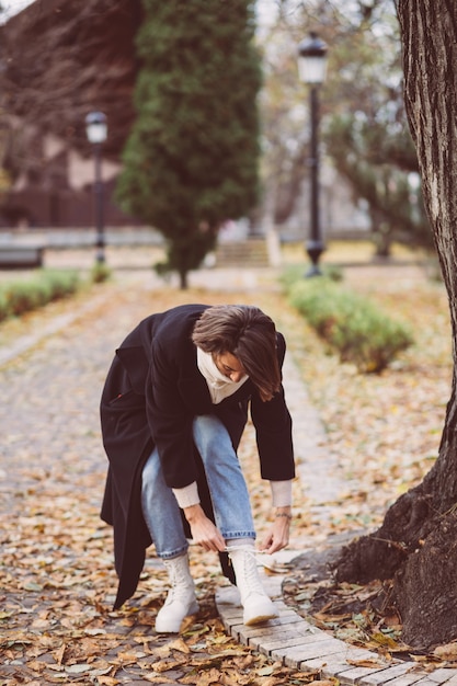 Openluchtportret van vrouw in park die zwarte winterjas en witte sjaal dragen