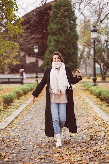 Openluchtportret van vrouw in park die zwarte winterjas en witte sjaal dragen