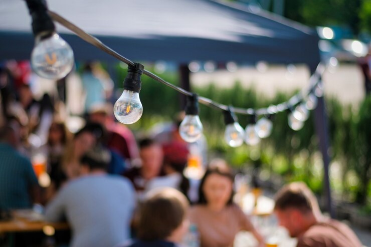 Opgehangen lampen bij buitenrestaurant met meerdere bezoekers op de achtergrond, BBQ