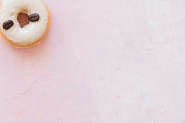Opgeheven mening van doughnut die met koffiebonen wordt verfraaid op roze achtergrond