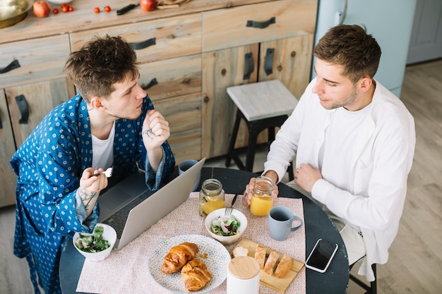 Opgeheven mening van mannelijke vrienden die ontbijt met sappen in keuken eten