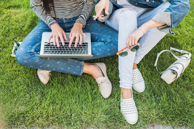Opgeheven mening van twee vrouwen die op groen gras zitten die laptop met behulp van