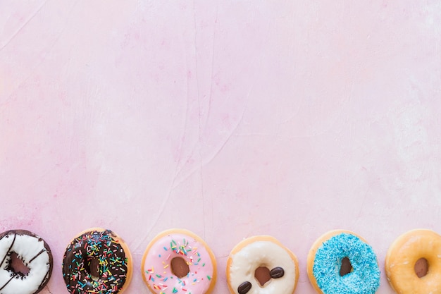 Opgeheven mening van verse donuts op een rij op roze achtergrond