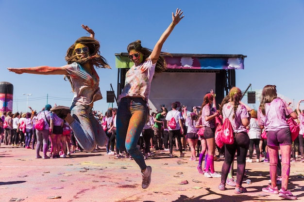 Opgewekte jonge vrouwen die in lucht springen die het holifestival vieren