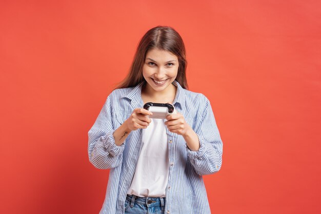 Opgewekte toevallige jonge vrouw die videospelletjes spelen die pret op rood hebben