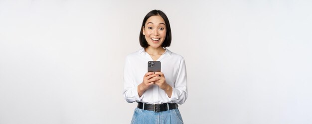 Opgewonden aziatische vrouw die lacht en reageert op info op een mobiele telefoon die een smartphone vasthoudt en er blij uitziet