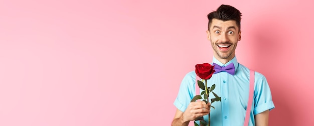 Gratis foto opgewonden bebaarde man met snor en vlinderdas wachtend op date met rode roos met romantisch moment
